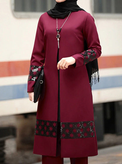 Maroon dress with black floral patterns worn by a person, standing on a platform.